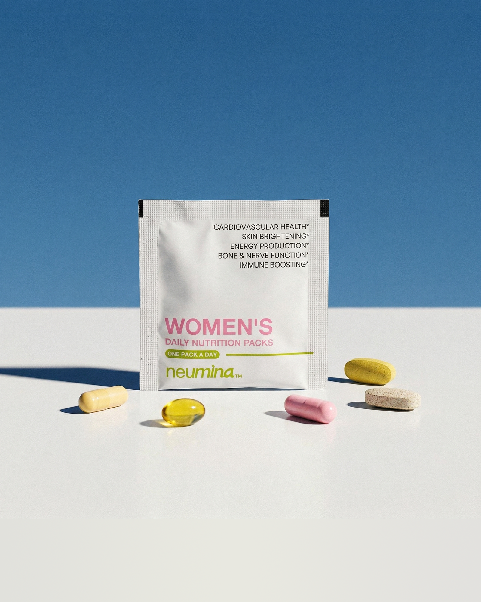 A minimalist lifestyle photo showing one Neumina Women's Daily Nutrition white sachet opened to reveal 5 distinct capsules and tablets. The stack includes a yellow softgel (fish oil), a pink capsule (beauty complex), and various multi-nutrient tablets. The packaging lists benefits such as Cardiovascular Health, Skin Brightening, Energy Production, Bone & Nerve Function, and Immune Boosting. Set against a clean blue and white background with modern hard shadows.