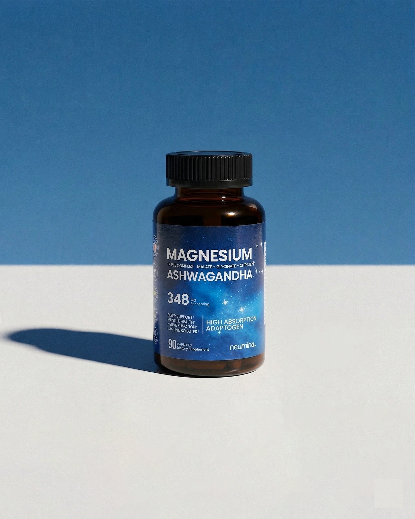 A high-quality lifestyle photograph of Neumina Magnesium Ashwagandha bottle set against a clean, two-tone blue and white background with a modern hard shadow. The label clearly displays "348mg per serving" and "High Absorption Adaptogen." This visual communicates a premium, simplified approach to magnesium supplementation for stress relief, muscle recovery, and sleep support, appealing to modern wellness-conscious consumers.