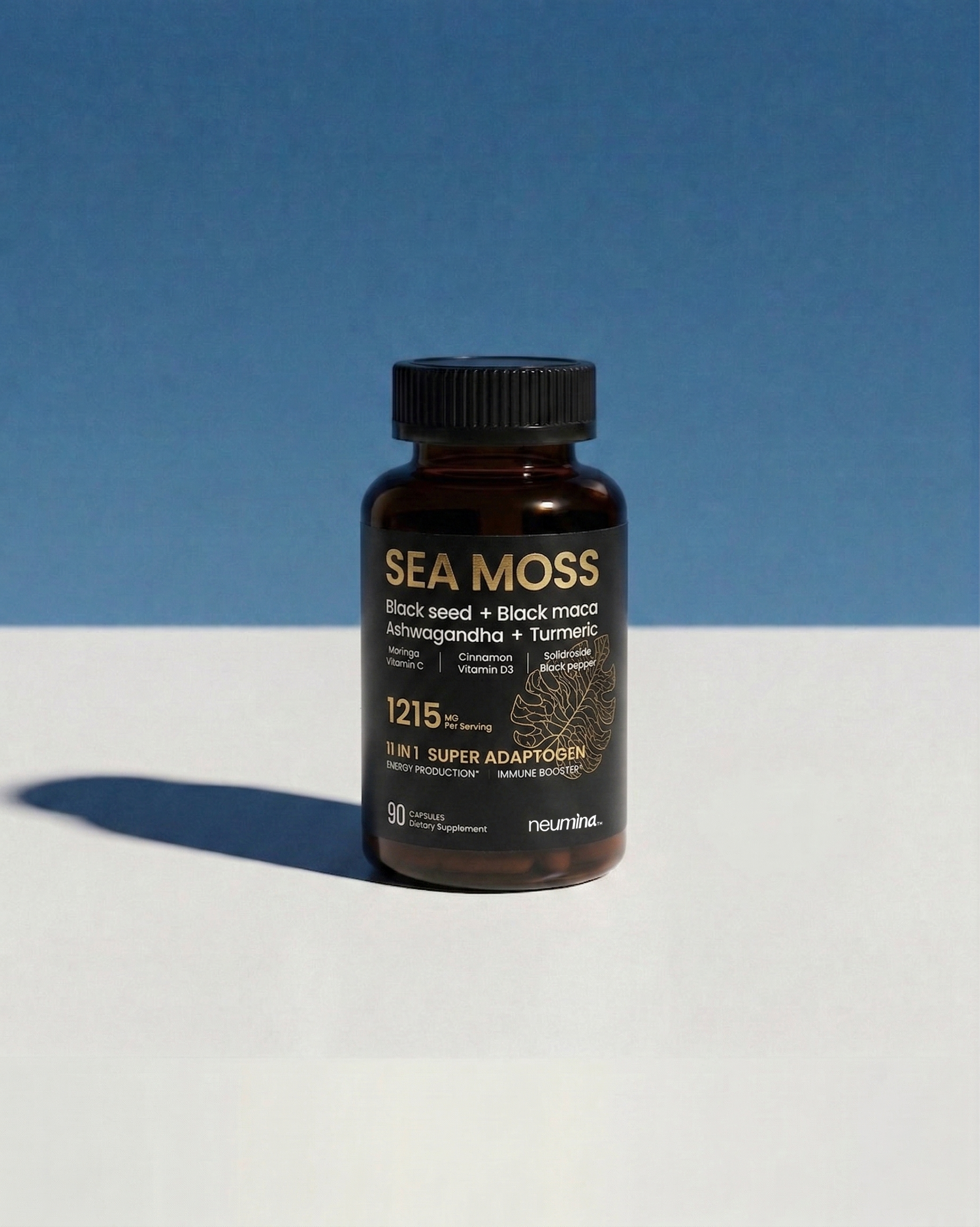 Product shot of Neumina brand Sea Moss 1215mg supplement. Bottle sits on a split blue and white background. Key terms on label include Black Seed, Ashwagandha, Turmeric, Black Maca, and 11-in-1 Super Adaptogen. Designed for minimalists looking for a comprehensive energy and immunity boost.