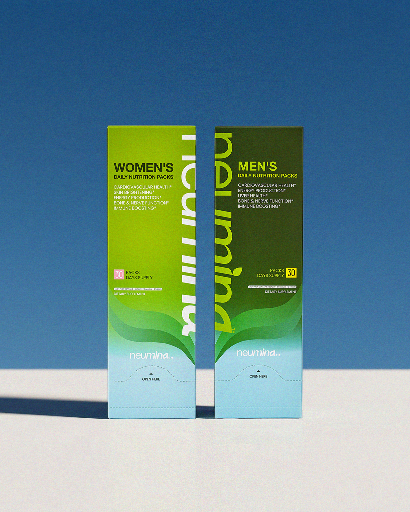 Authentic studio shot of Neumina Women's and Men's Daily Nutrition Packs in bright natural lighting. Showcases two sleek dispenser boxes (30-day supply each) designed for gender-specific health optimization. Women's pack: Skin brightening and energy. Men's pack: Liver health and stamina. Features minimalist branding and a convenient "Open Here" mechanism. Focus: high-end lifestyle multivitamin bundle and premium family health gift idea.