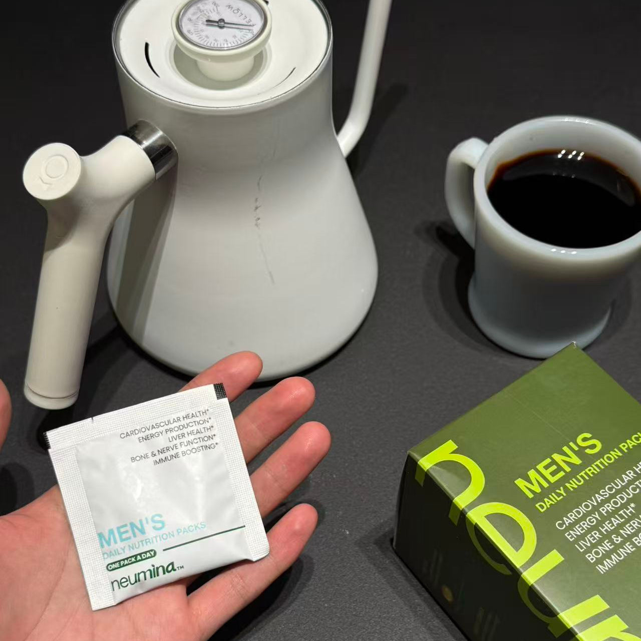 Neumina hand holding Men's Daily Nutrition Pack next to morning coffee - wellness vitamins for energy and immune support